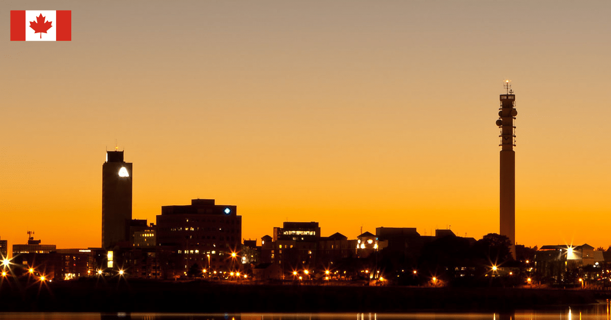 Moncton skyline silhouetted against an orange sunset sky with illuminated buildings reflecting on calm water